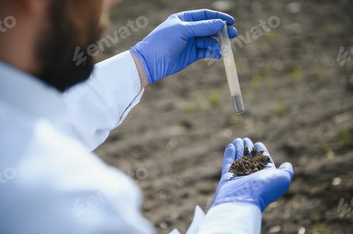 Preview: Laboratory worker holding professional glassware and testing black soil after harvest in the field