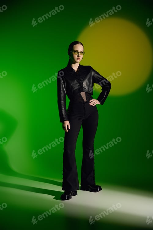 Preview: Stylish young woman poses confidently in black outfit against vibrant green backdrop