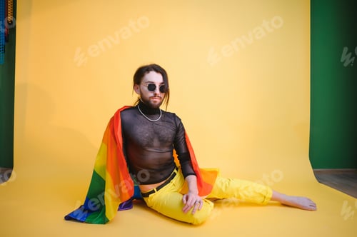 Preview: gay man with a gay pride flag smiling and looking away on yellow background