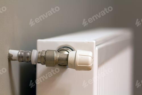 Preview: White metal heating radiator mounted on gray wall inside a room.