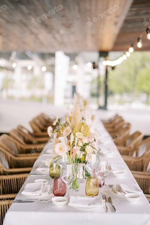 Preview: Bouquets of flowers stand on a long festive table with wicker chairs around