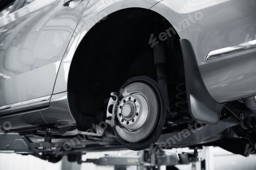 Preview: Modern car on hydraulic lift at automobile repair shop, closeup