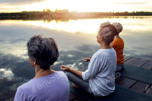 Preview: Group of senior woman doing yoga exercises by the lake.