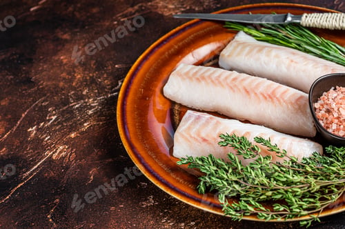 Preview: Raw cod loin fillet steaks on rustic plate with thyme and salt. Dark background.