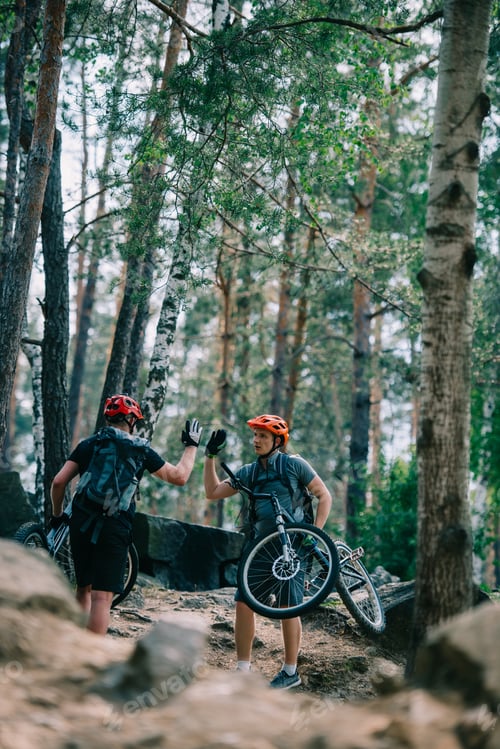 Preview: young trial bikers giving high five at beautiful forest