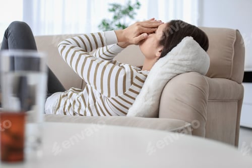 Preview: Young woman suffering from headache on sofa at home