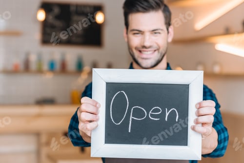 Preview: portrait of smiling barista showing chalkboard with open word in hands in cafe