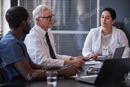 Preview: Female Clinical Doctor Listening to Senior Colleague while Diagnosing Disease at Meeting Table