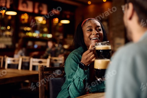 Preview: Happy black woman and her friend toasting with beer in a pub.