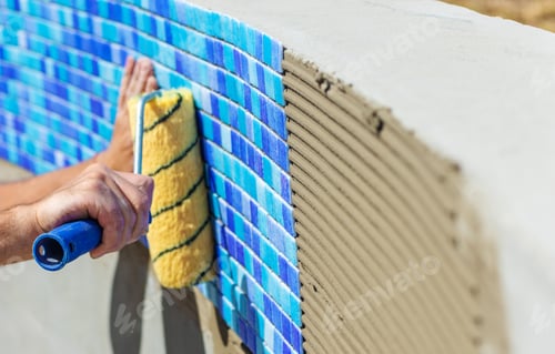 Preview: A man lays mosaic tiles in a swimming pool. Selective focus.