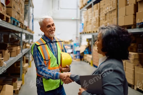 Preview: Happy senior warehouse worker greeting his manager at storage compartment.