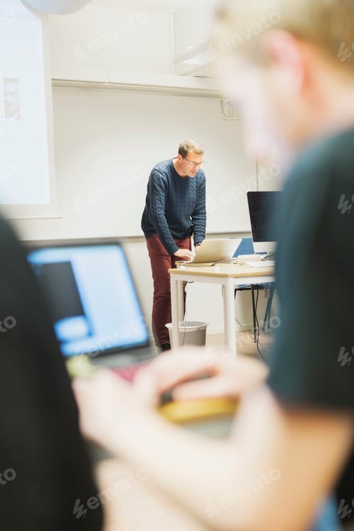 Preview: Teacher using laptop at desk in media classroom
