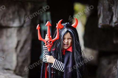 Preview: Happy little Caucasian girl wearing costume of evil with red horns and long brunette hair outdoor