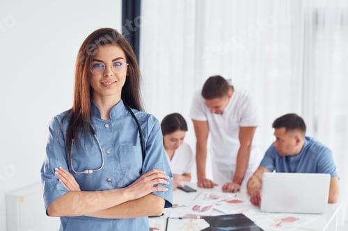 Preview: Woman standing against group of young doctors that is working together in the modern office