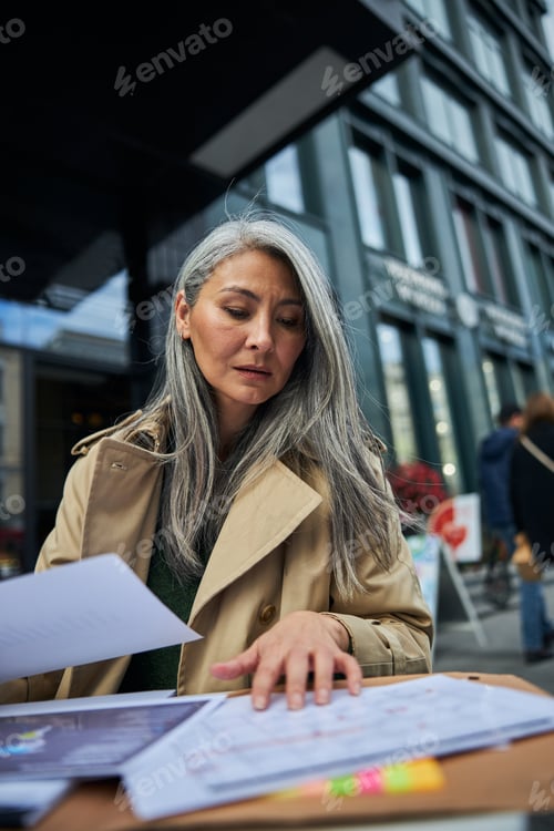Preview: Serious businesswoman working with documents in outdoor cafe