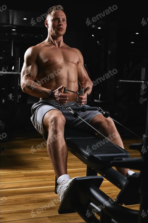 Preview: Side view of a strong young man with athletic body doing exercises on fitness equipment in a dark