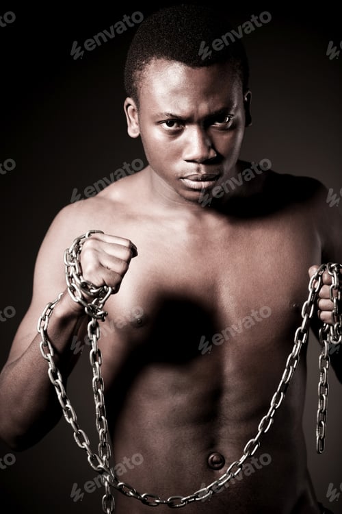 Preview: Young half naked african man standing and holding massive chains in hands