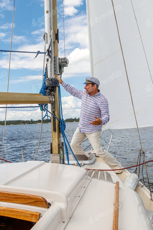 Preview: sailor man in a cap on a boat under sail against the sky and water