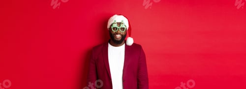 Preview: Funny Black man in santa hat and party glasses celebrating Christmas, smiling happy and wishing