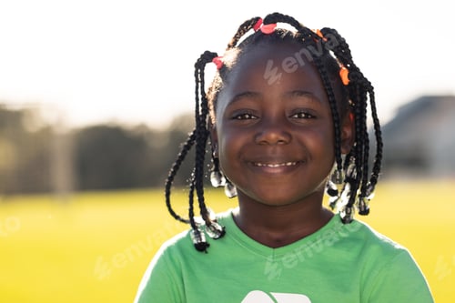 Preview: Portrait of african american schoolgirl smiling in sunny elementary school sports field, copy space