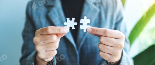 Preview: Closeup image of a businesswoman holding and putting a piece of white jigsaw puzzle together
