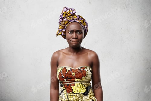 Preview: Desperate dark-skinned woman in elegant dress and scarf pressing her lips being nervous. Black beaut