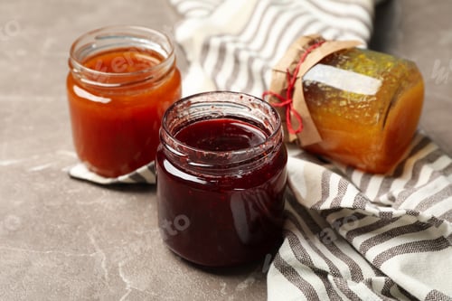 Preview: Napkin and glass jars with jam on gray background, close up