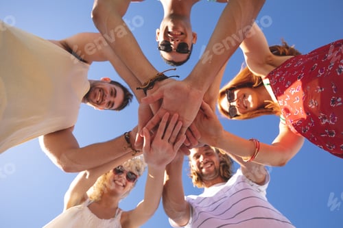 Preview: Portrait of group of young diverse friends forming hand stack on the beach