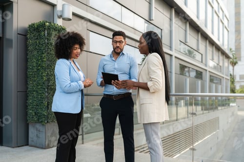 Preview: Three Multiracial business people discussing work strategy using a digital tablet outside office
