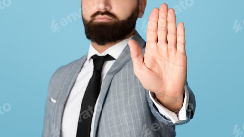 Preview: Cropped view of millennial businessman refusing something, showing STOP gesture on blue studio