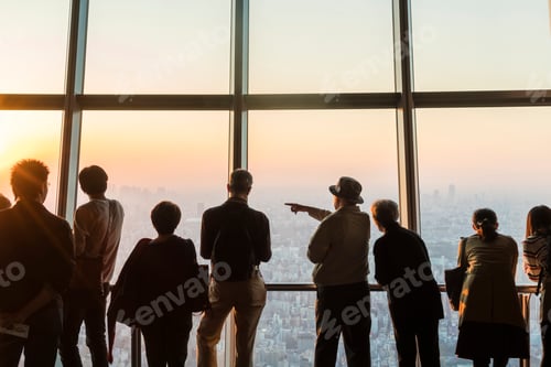 Vorschau: Rückblick-Silhouette einer Gruppe von Menschen, die vom Wolkenkratzerfenster aus auf das Stadtbild blicken.