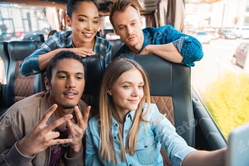 Preview: happy multiethnic friends taking selfie on smartphone during trip on travel bus