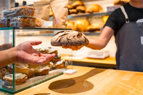 Preview: Customer hands in the bakery shop buying an artisan bread from the baker in the workshop workshop