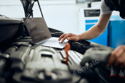 Preview: Close-up of auto mechanic using laptop while examining car engine in repair shop.