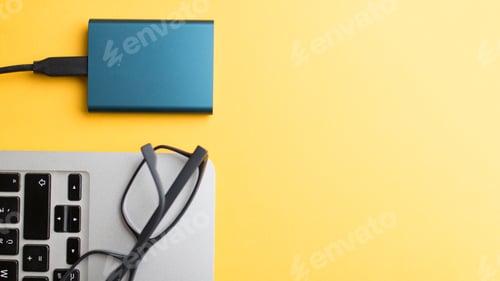 Preview: Closeup of a notebook with a power bank attached and glasses