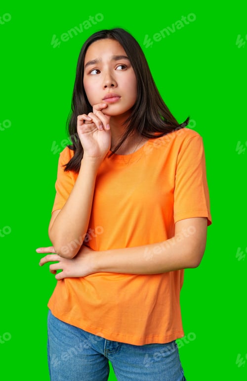 Preview: Young woman in orange shirt poses thoughtfully with green background