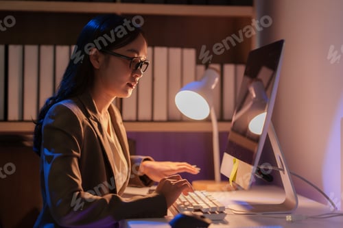 Preview: Focused asian businesswoman working late at night in office typing on computer keyboard