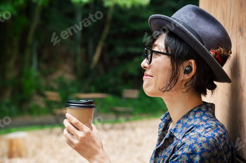 Preview: Japanese woman wearing glasses and hat standing outside Eco Cafe, holding paper cup.
