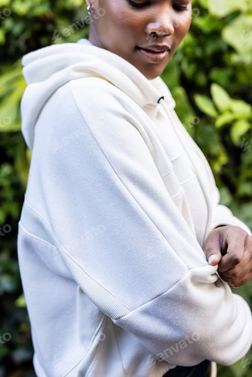 Preview: Happy african american woman wearing white hooded sweatshirt touching sleeve in garden