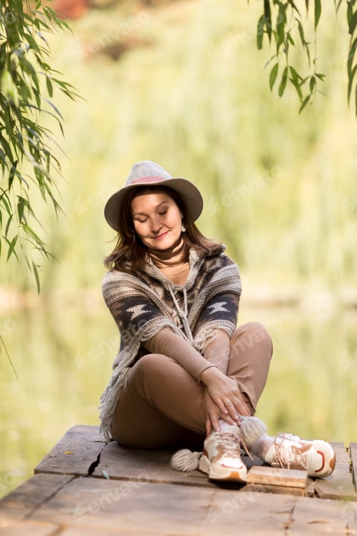 Preview: fashionable beautiful woman sitting on the bridge on the lake in autumn