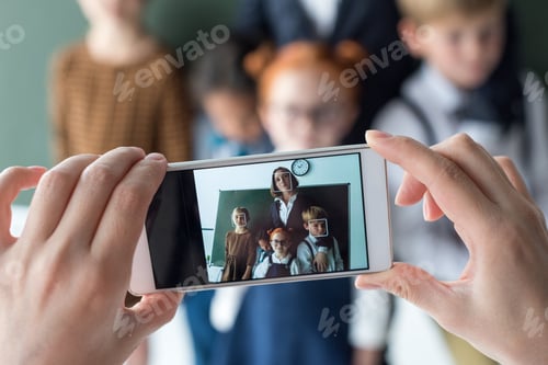 Preview: close-up view of young female teacher and cute little students photographing with smartphone