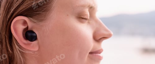 Preview: Woman using wireless earpieces, seaside on the background