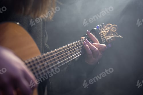 Preview: Close-up of female hands playing acoustic guitar in the dark.