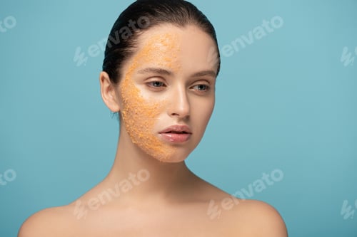 Preview: attractive girl applying yellow sugar exfoliant on face, isolated on blue