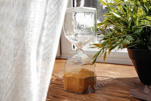 Preview: Hourglass with golden sand pouring inside on wooden background