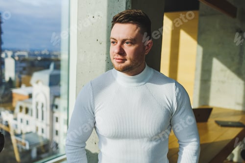 Preview: A young handsome man in a white sweater is standing in a spacious bright office