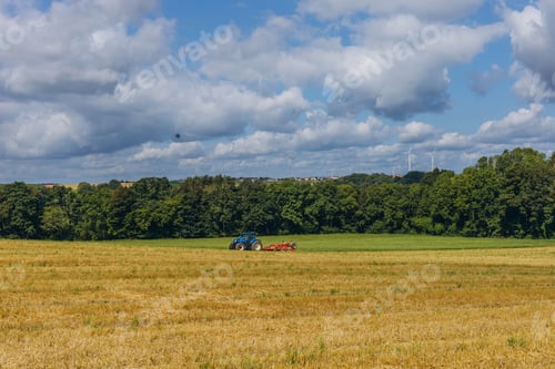 Preview: Agricultural machinery drives across field. Big tractor. SIder view. White cumulus clouds background
