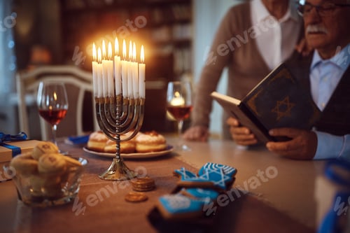 Preview: Lit candles in menorah with Jewish couple reading Hebrew bible in the background.