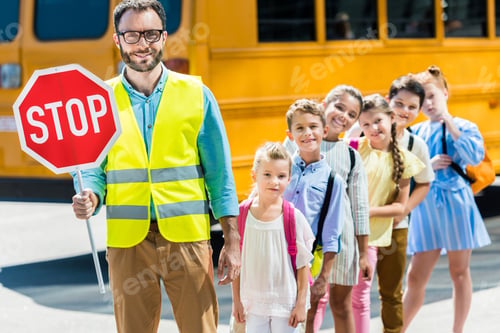 Preview: miling traffic guard with scholars looking at camera in front of school bus