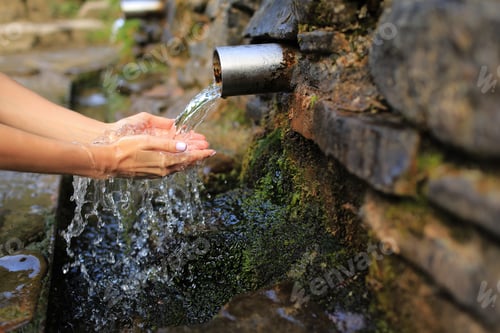 Preview: Woman collect pure water in hand palm from the source in the wall, hold and drink it.